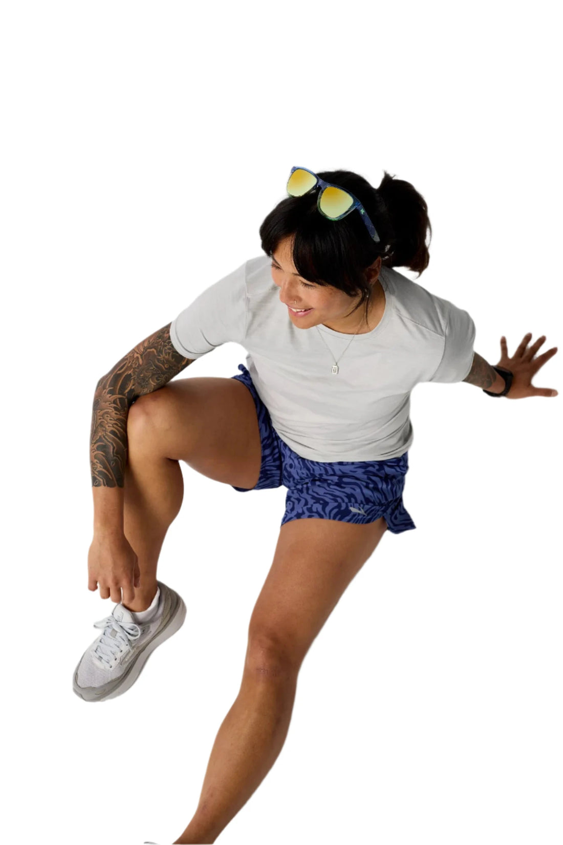 Person sitting on a white surface wearing a white shirt, blue patterned shorts, and gray sneakers.