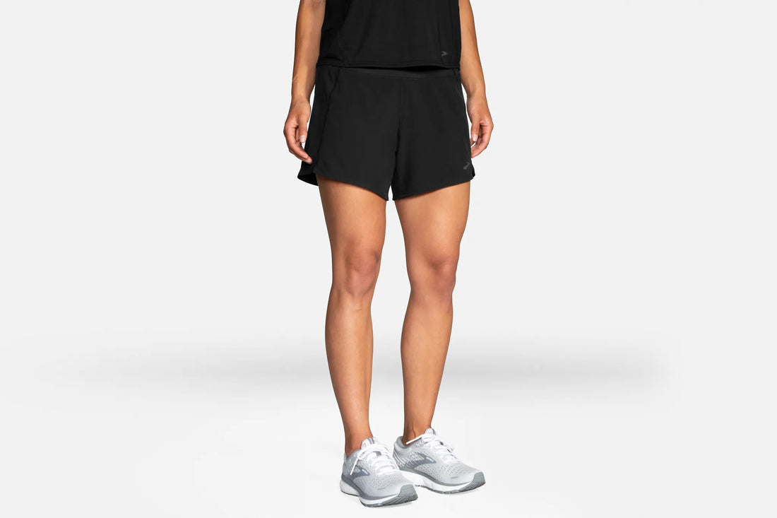 Person wearing black athletic shorts and white sneakers on a light gray background